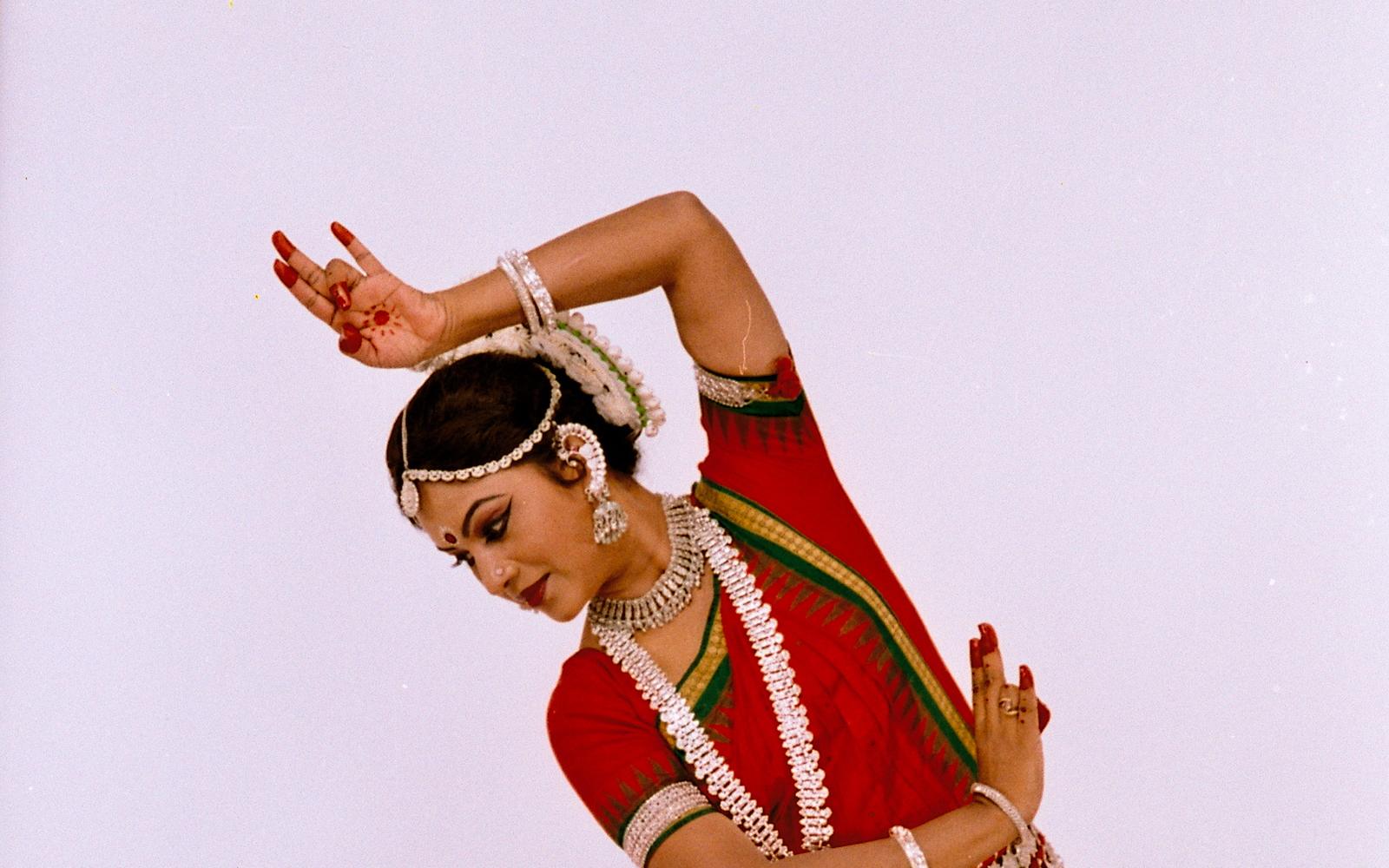 Shubhada Varadkar in a red Odissi costume, one arm curved above her head.