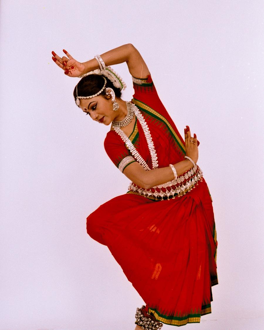 Shubhada Varadkar in a red Odissi costume, one arm curved above her head.
