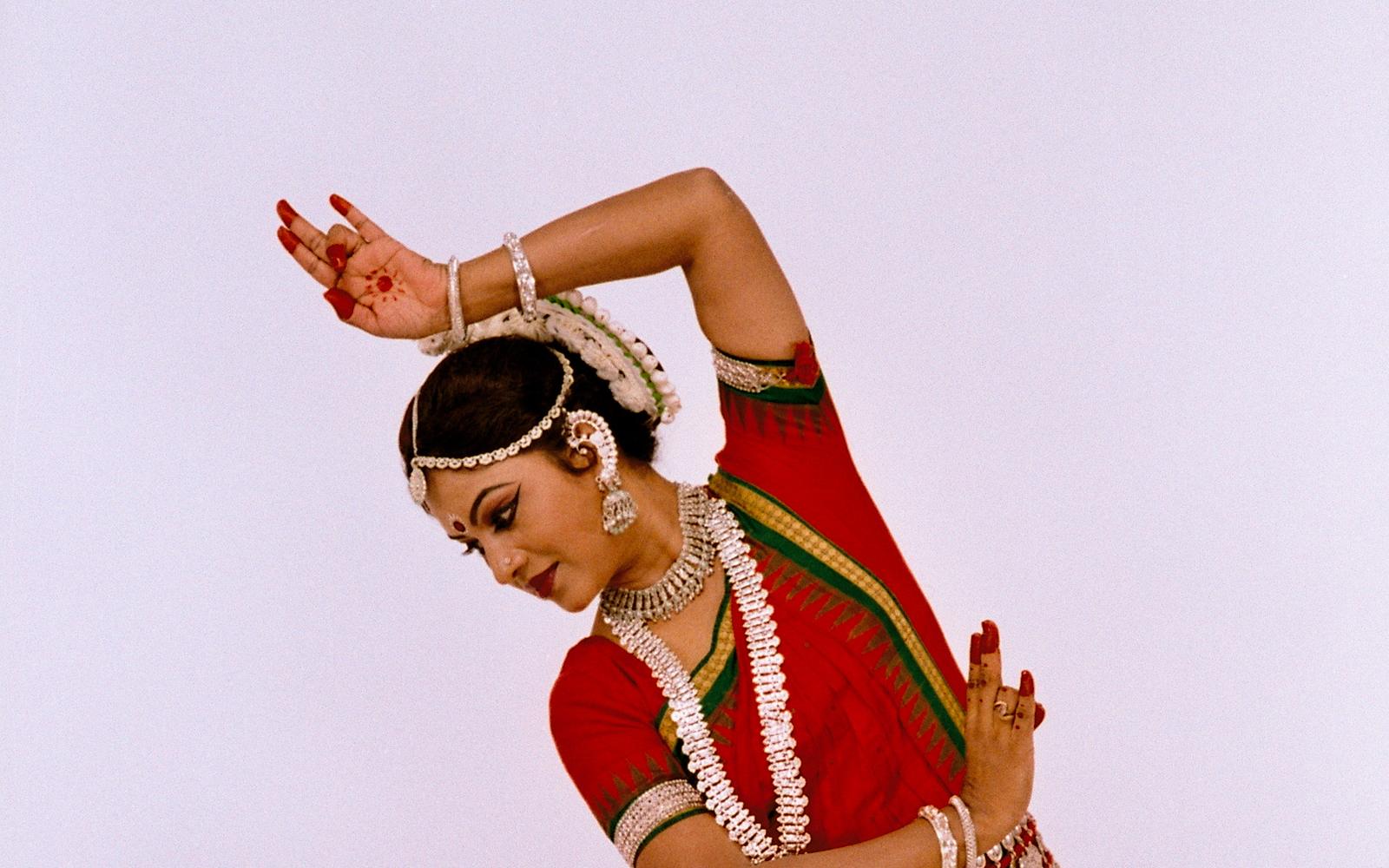 Shubhada Varadkar in a red Odissi costume, arm raised in a dance posture.