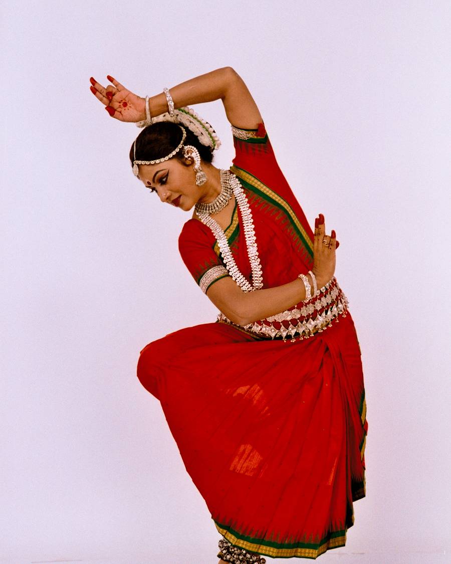 Shubhada Varadkar in a red Odissi costume, arm raised in a dance posture.