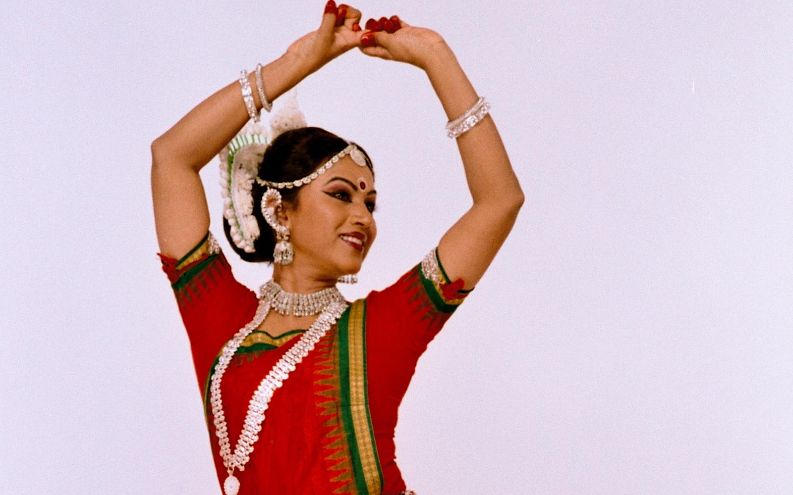 Shubhada Varadkar with both arms raised overhead in an Odissi pose.