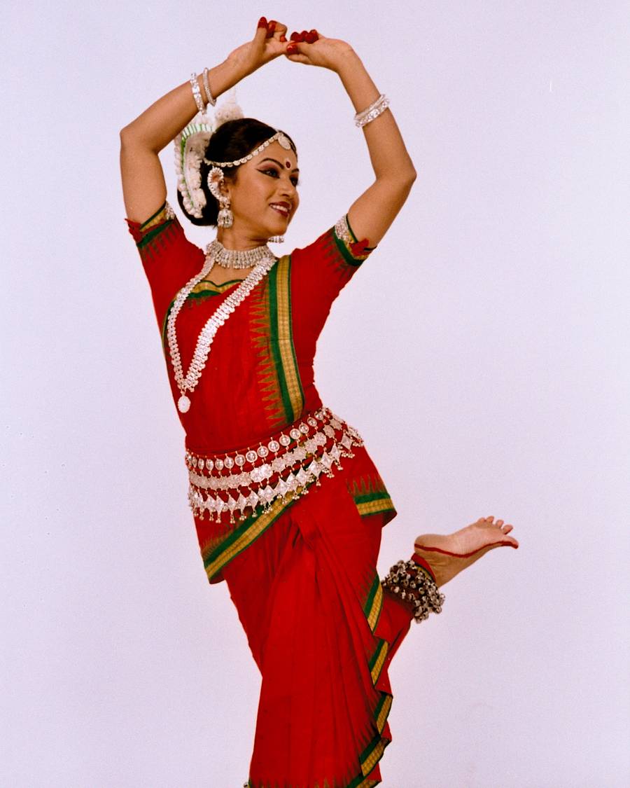 Shubhada Varadkar with both arms raised overhead in an Odissi pose.