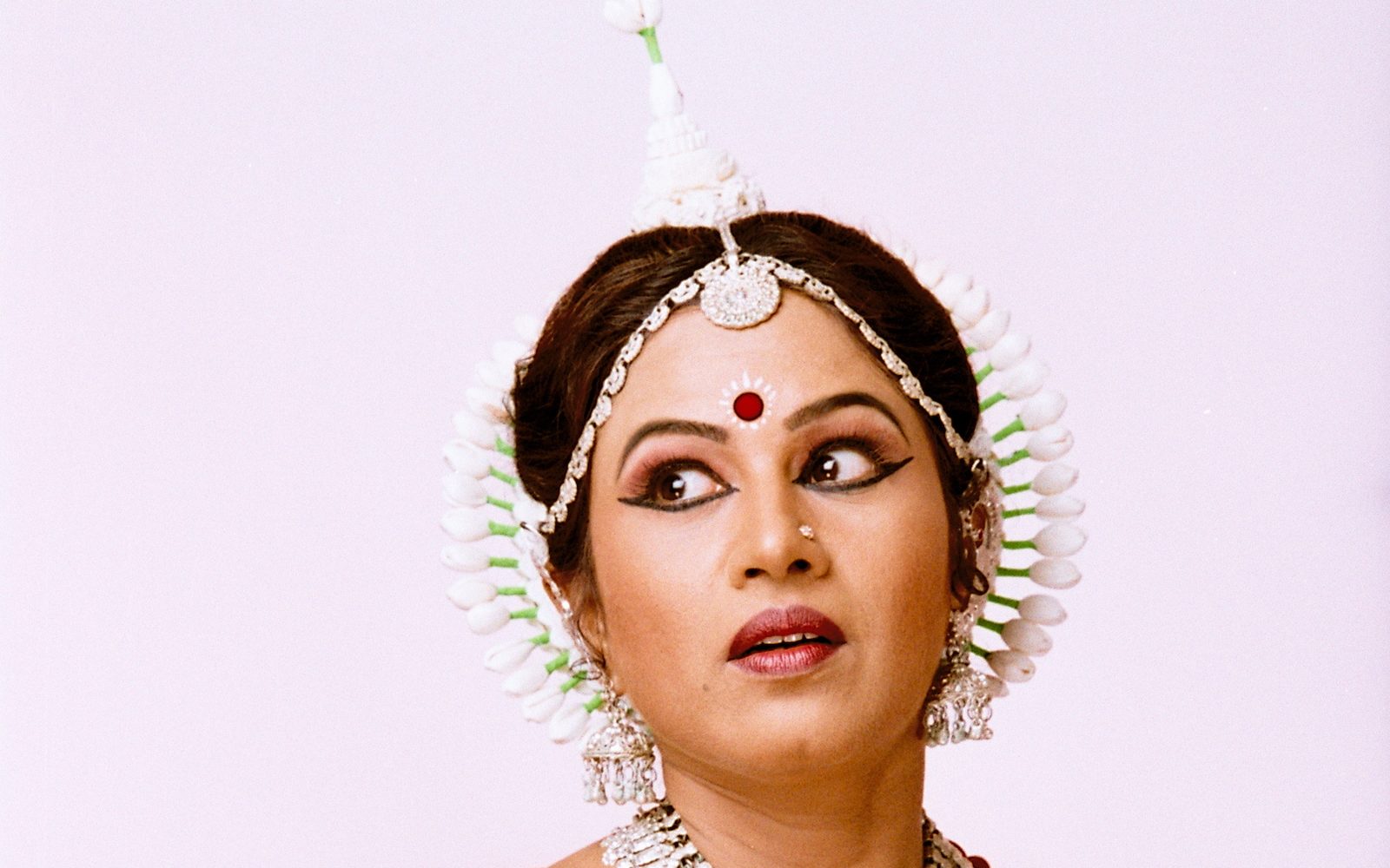 Shubhada Varadkar in an orange and red Odissi costume, gaze turned aside.