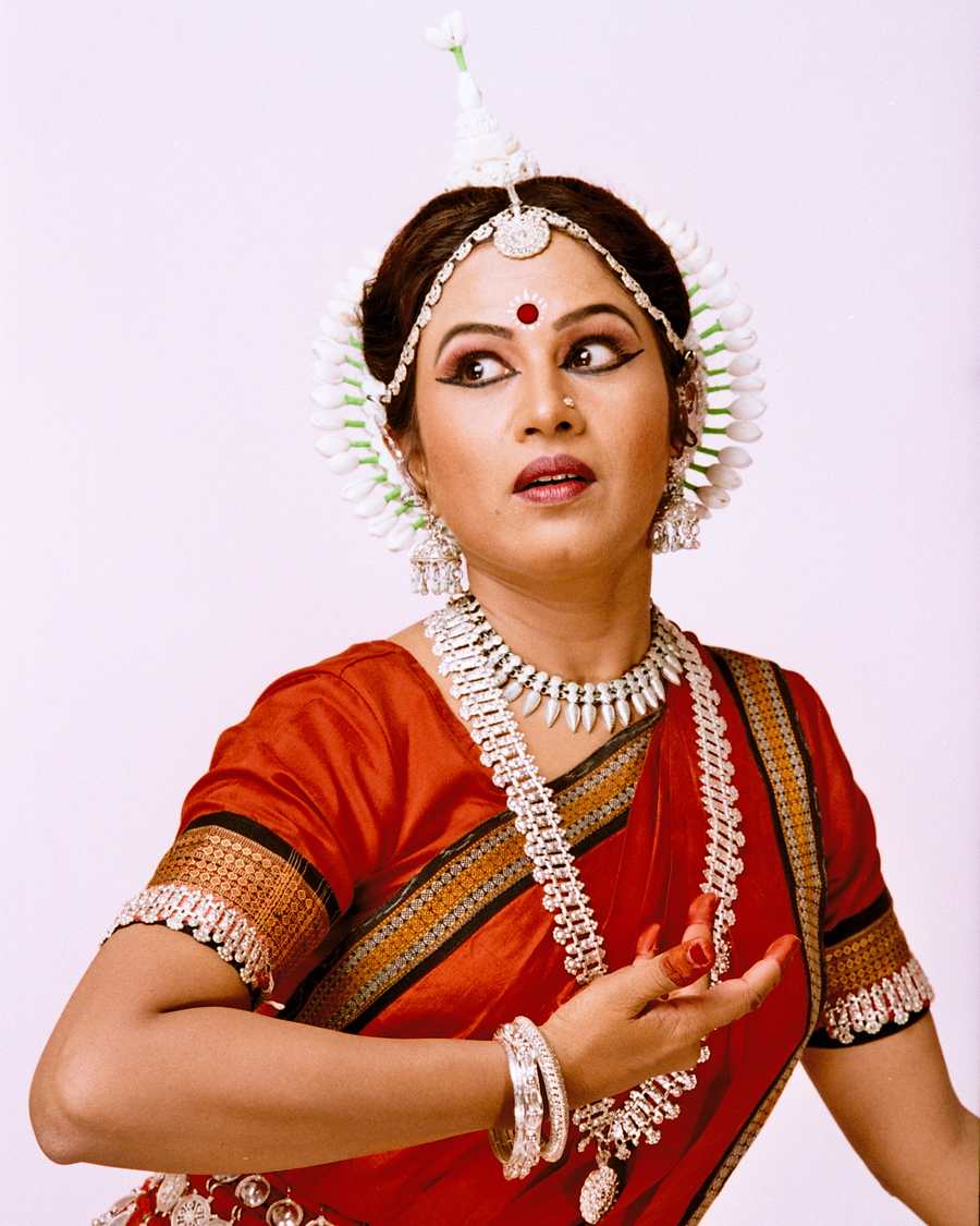 Shubhada Varadkar in an orange and red Odissi costume, gaze turned aside.