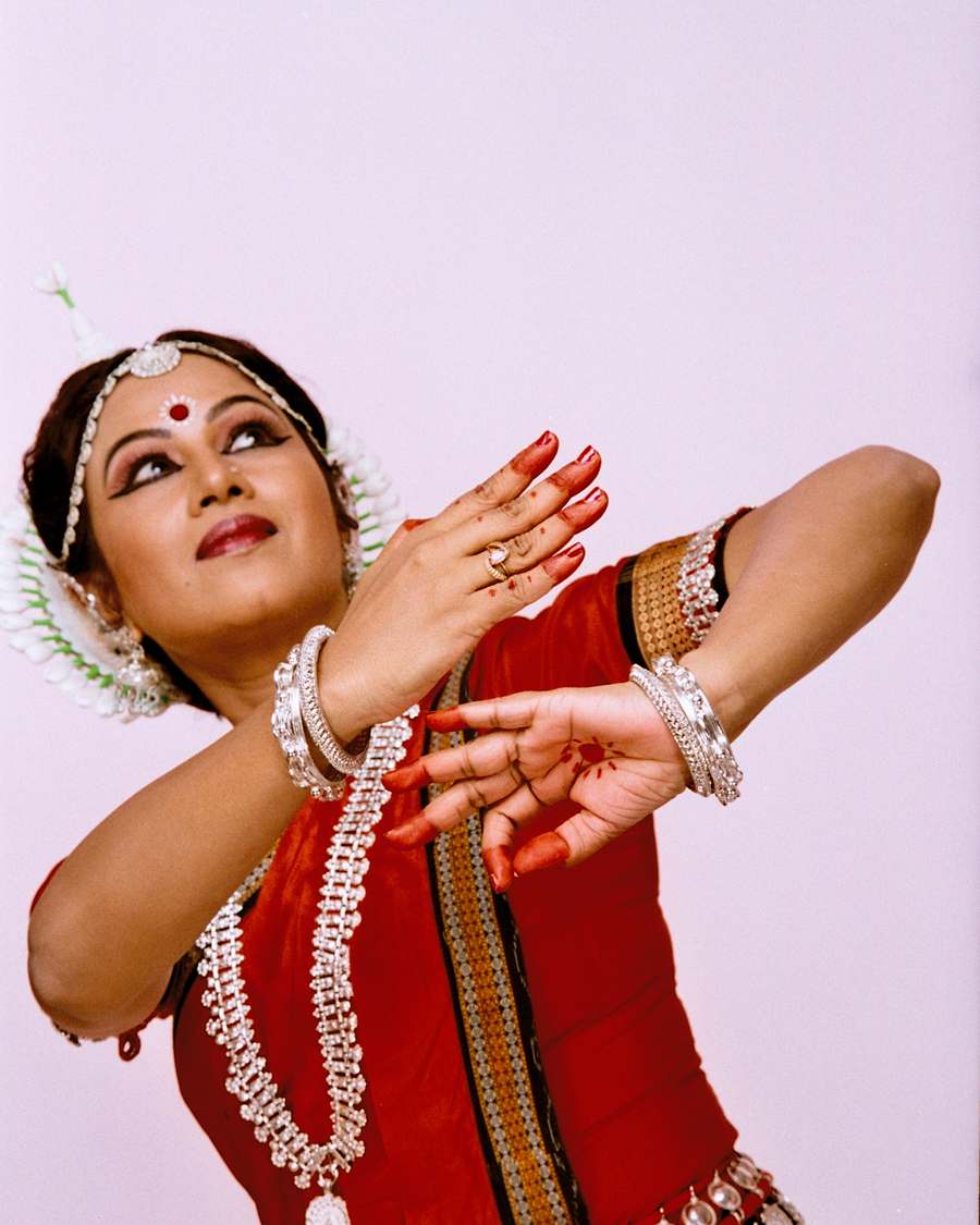 Shubhada Varadkar in a red Odissi costume, arms extended and gaze lifted.