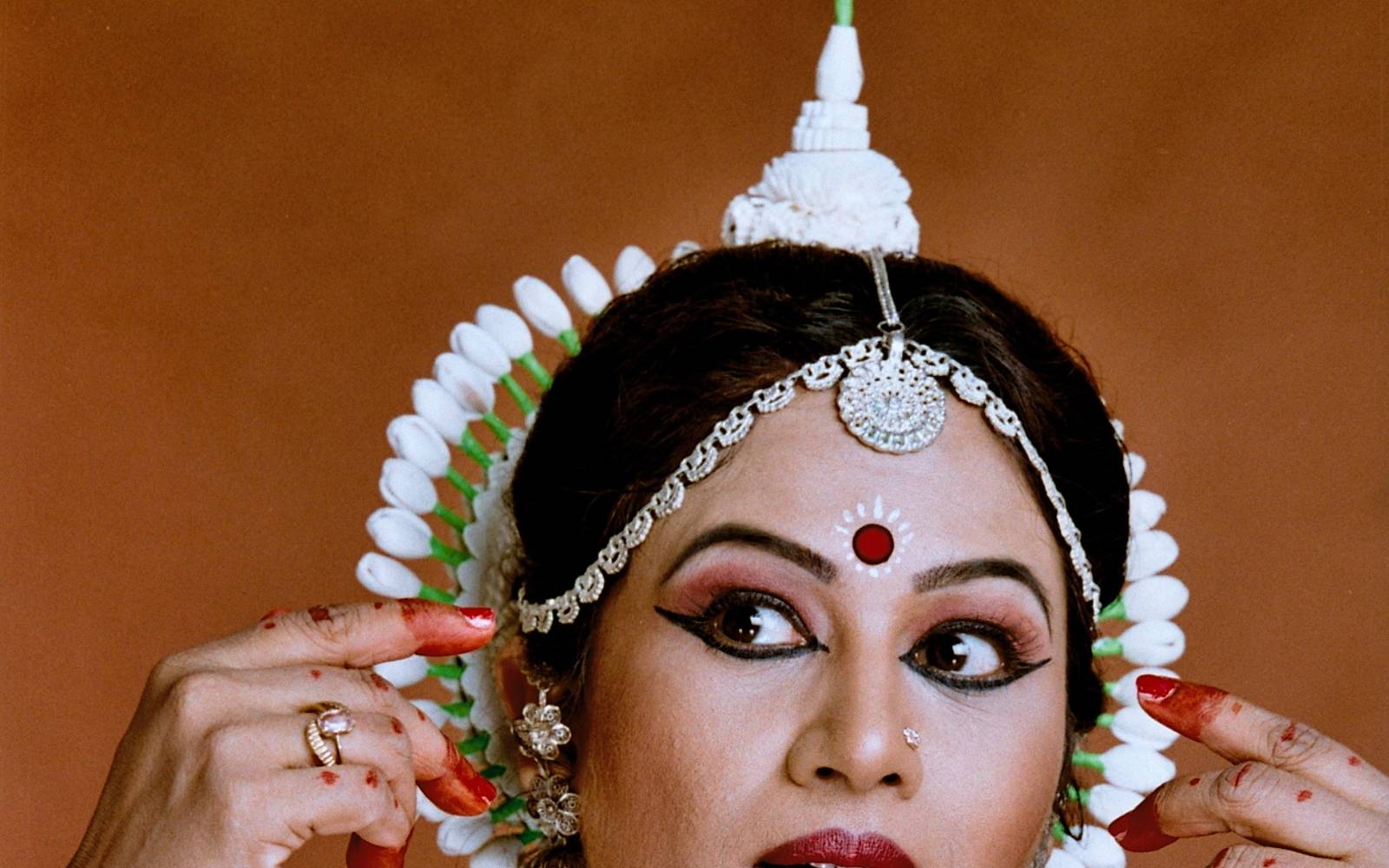 Shubhada Varadkar in white and red Odissi costume, hands at her headdress.