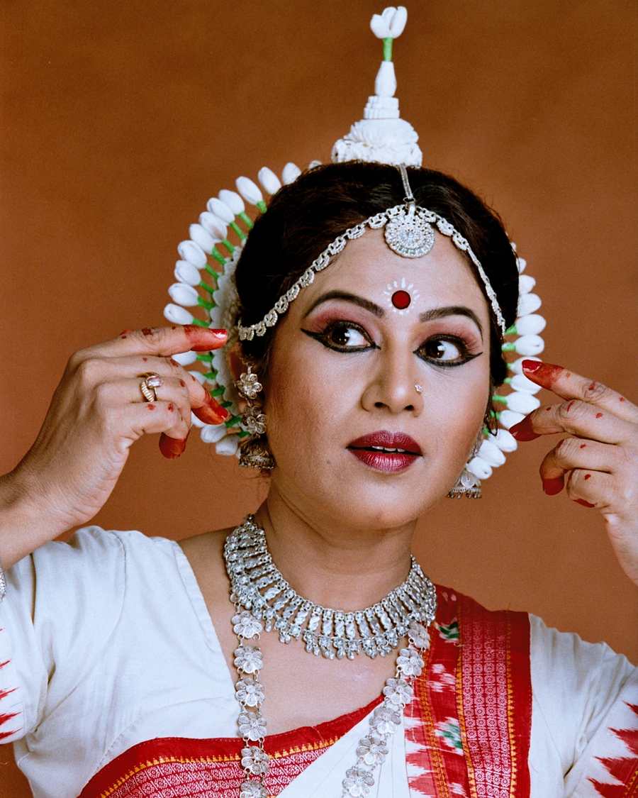 Shubhada Varadkar in white and red Odissi costume, hands at her headdress.